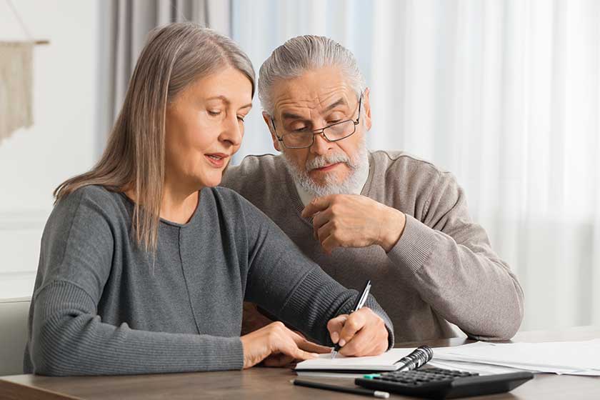 Elderly couple with papers discussing pension plan at wooden table indoors