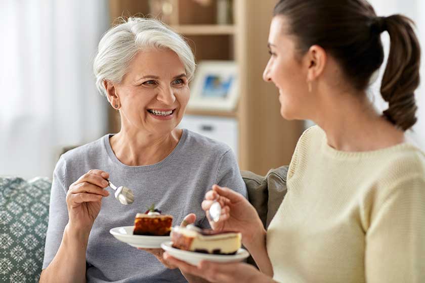 Old mother and adult daughter eating cake at home