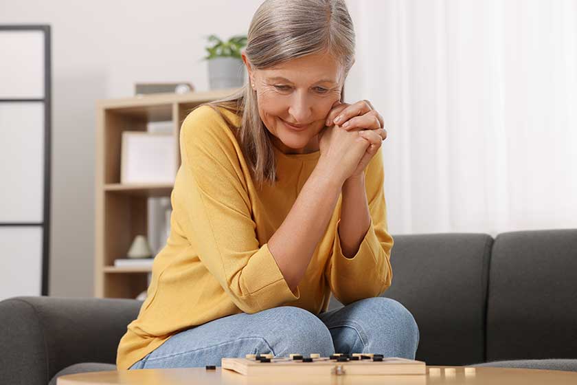 Thoughtful senior woman playing checkers at home